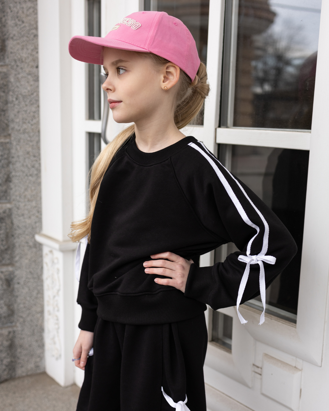 Girl wearing black bow sweatshirt from Alwair Kids standing outside – side view.