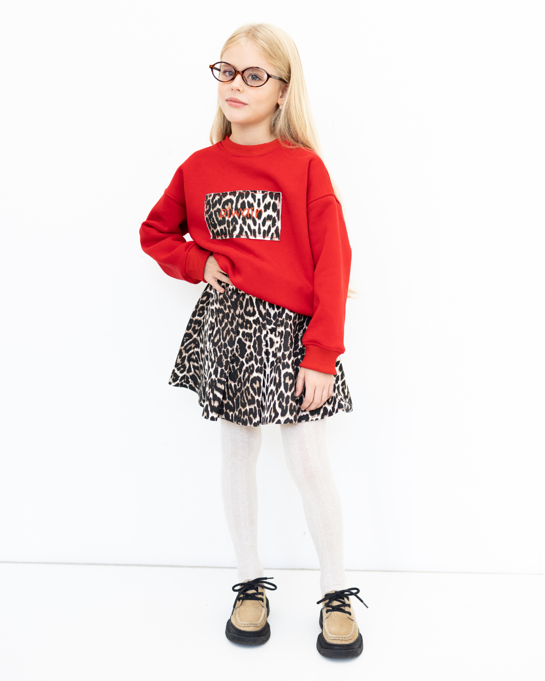 Girl wearing red sweatshirt and leopard denim skirt from Alwair Kids Leo capsule collection, front pose with hand on hip