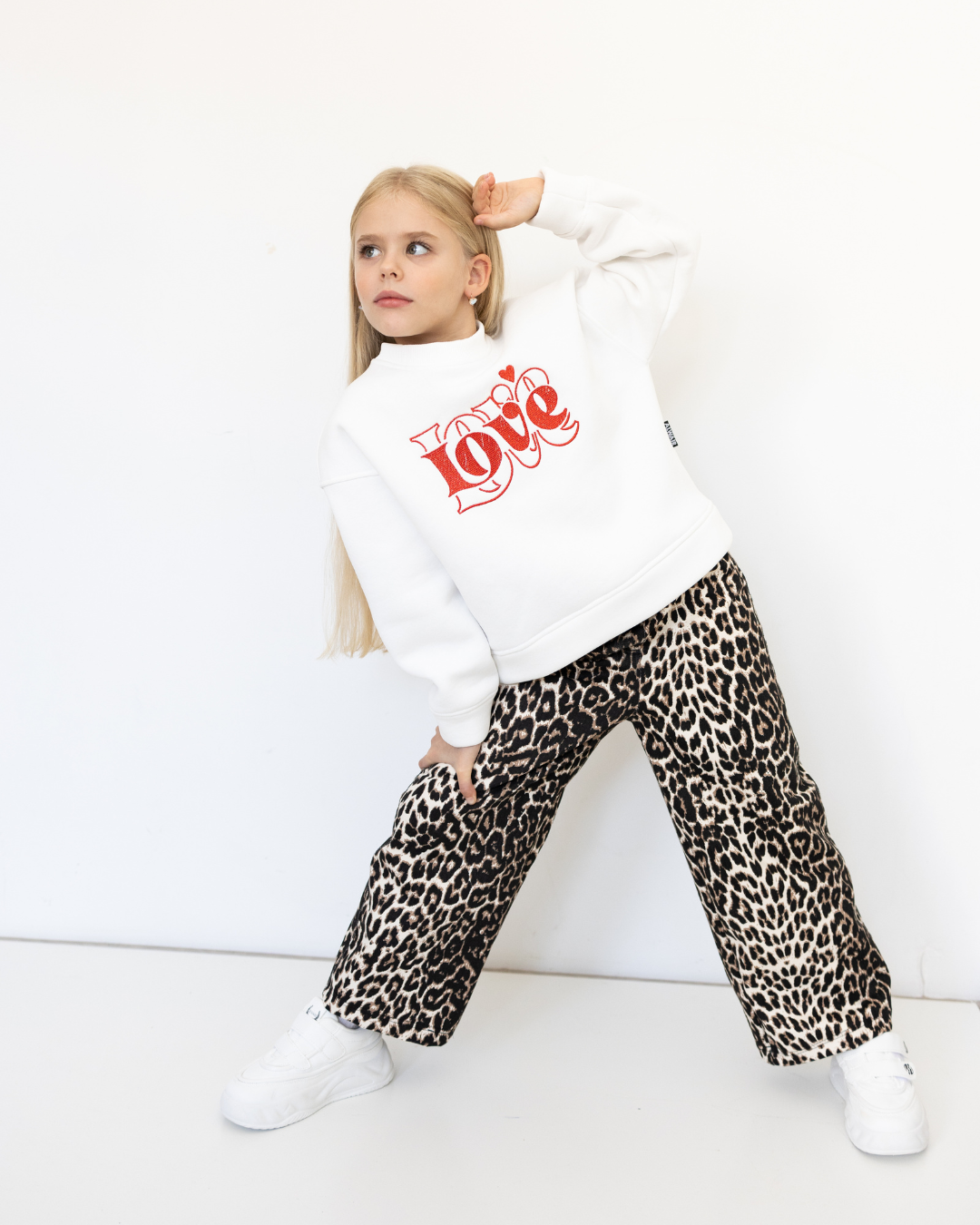 Girl posing in dynamic stance wearing white Love print sweatshirt