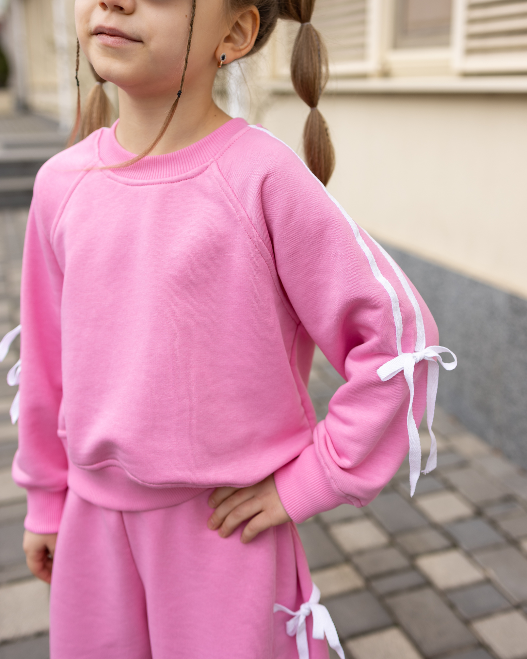 Young girl in pink Alwair Kids bow sweatshirt posing with hand on hip – close-up.