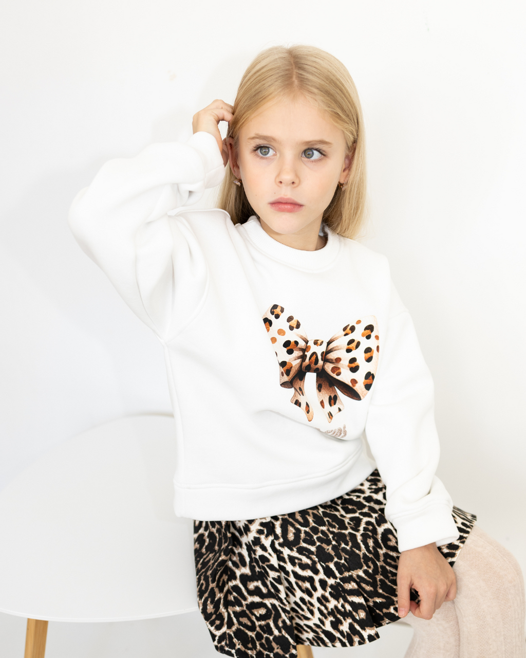 Cute girl in Alwair Kids leopard bow sweatshirt sitting on a chair
