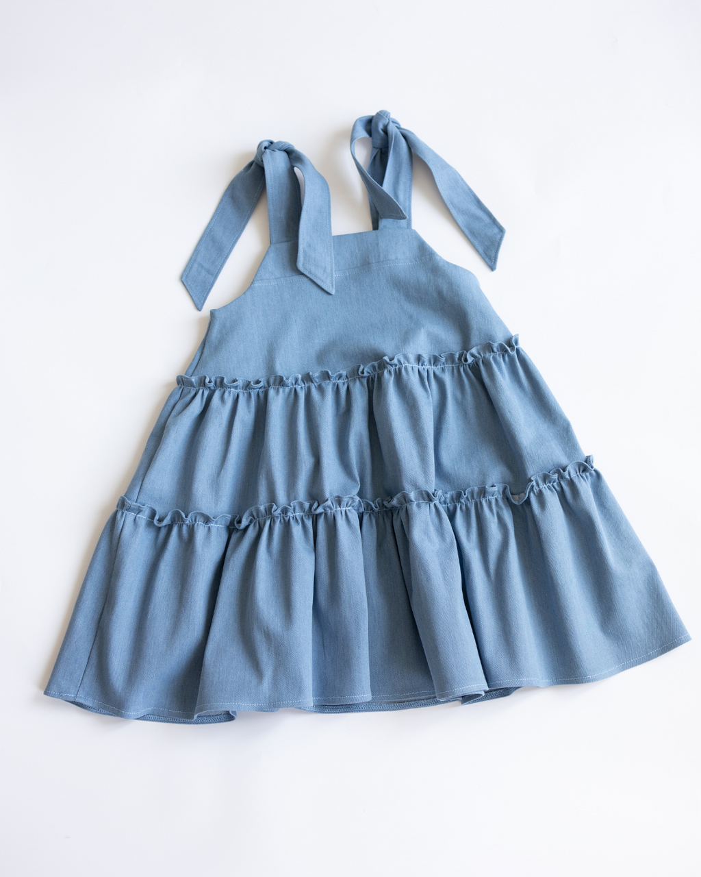 Back view of tiered girls’ denim sundress with tie straps
