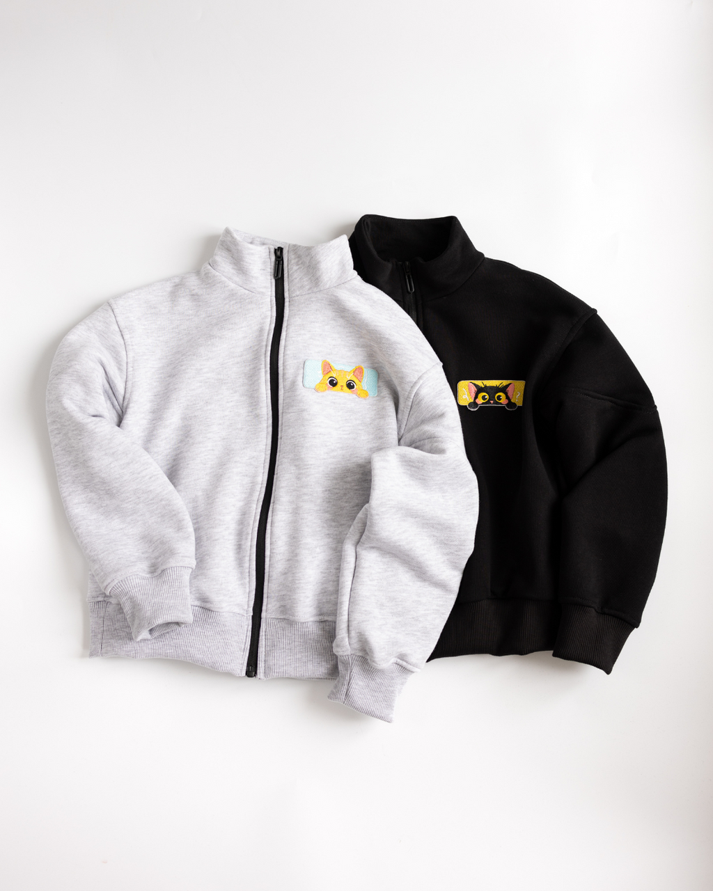 Front view of Alwair Kids cotton zip-up jackets in black and grey with cat patches


