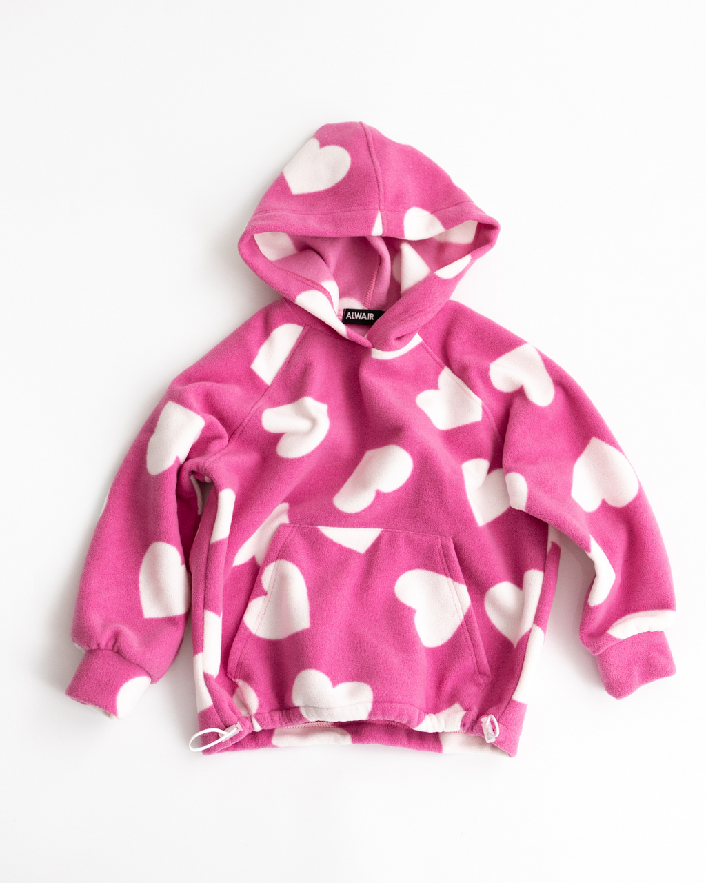 Flat lay of pink fleece hoodie with white hearts and adjustable hem

