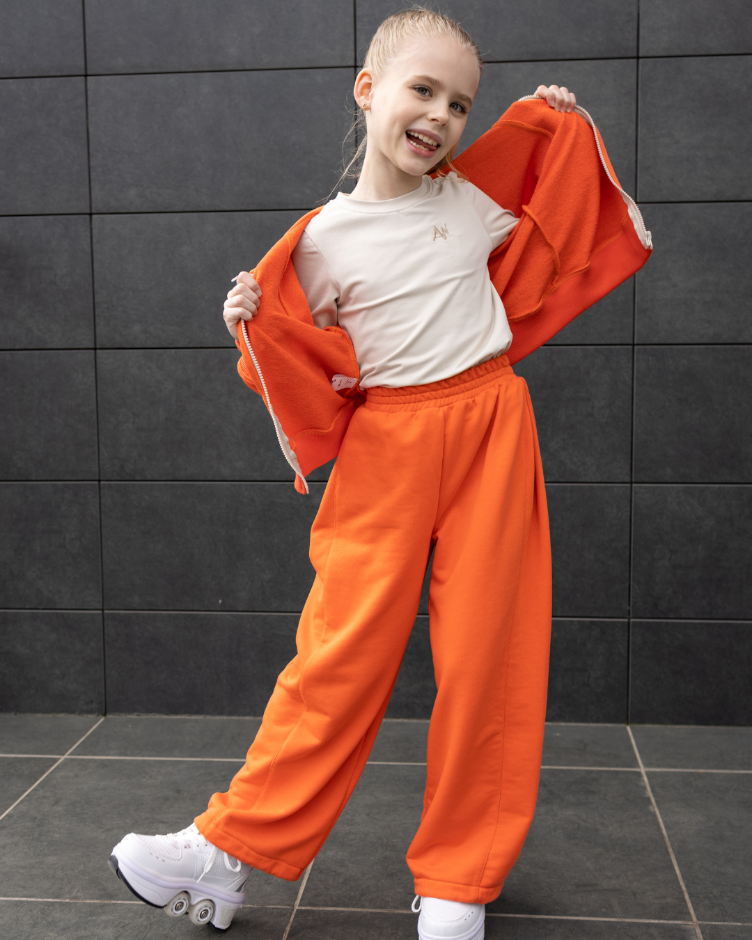 Active girl in Alwair Kids orange tracksuit showing long sleeve and drawstring pants