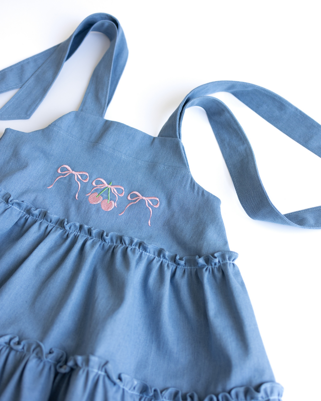 Close-up of cherry embroidery and ruffle detailing on denim sundress
