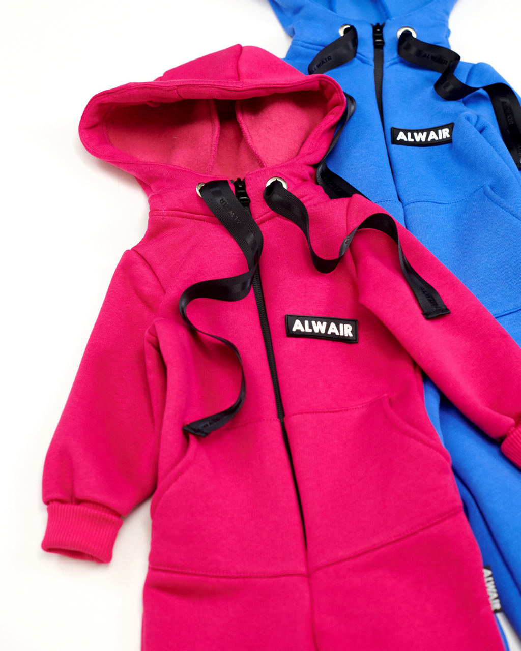 Close-up of pink and blue fleece kids jumpsuits with Alwair logos and ribbon details