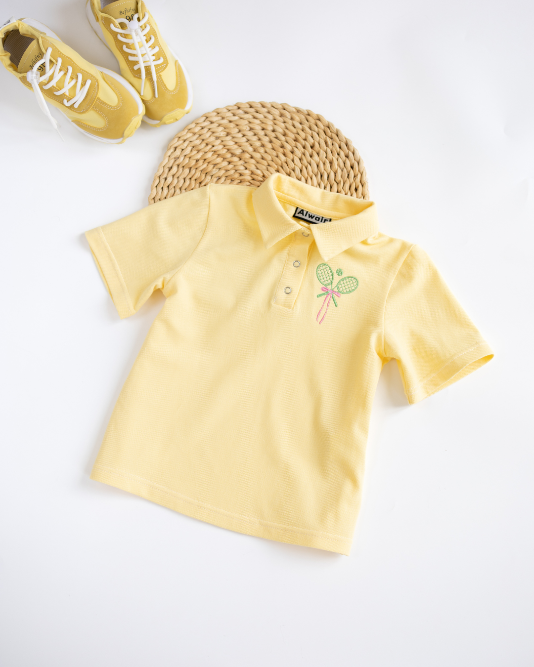 Flat lay of yellow Alwair Kids tennis polo shirt with yellow shoes