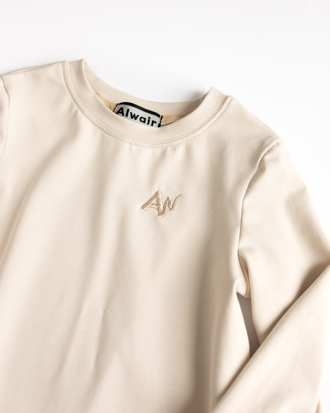 Close-up of embroidered logo on beige Alwair Kids girls top

