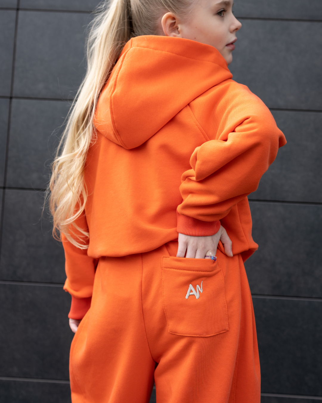 Back view of orange Alwair Kids tracksuit highlighting branded pocket design

