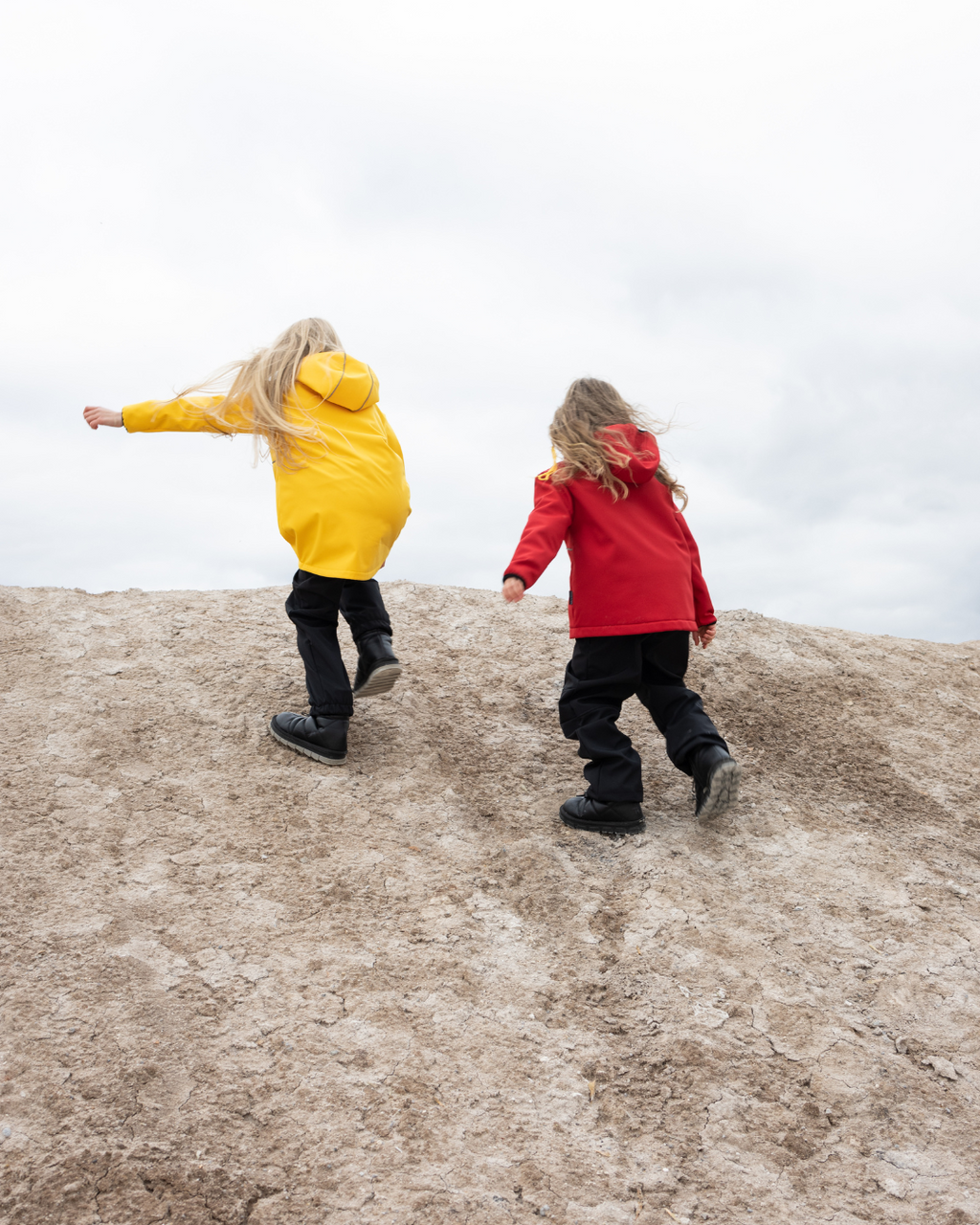 Back view of two girls running uphill in yellow and red softshell jackets by Alwair Kids

