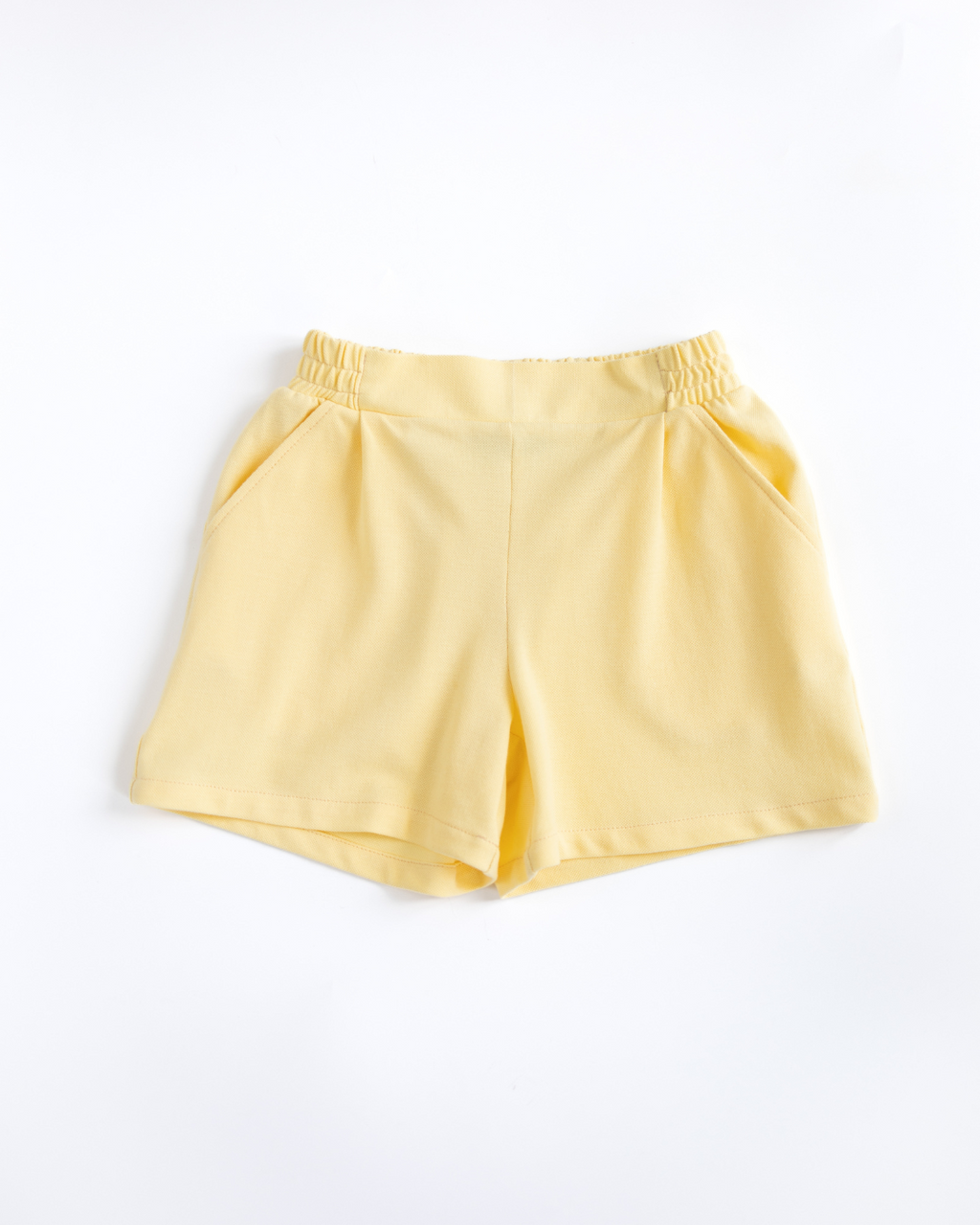 Flat lay yellow lacoste girls shorts with elastic waistband and side pockets