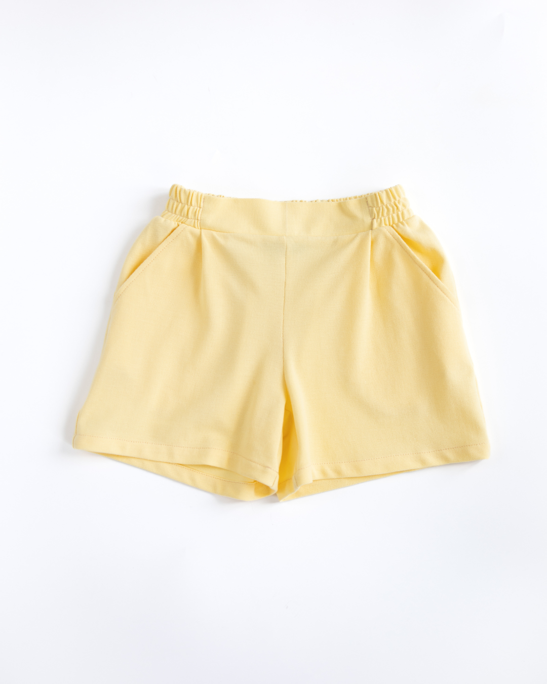 Flat lay yellow lacoste girls shorts with elastic waistband and side pockets