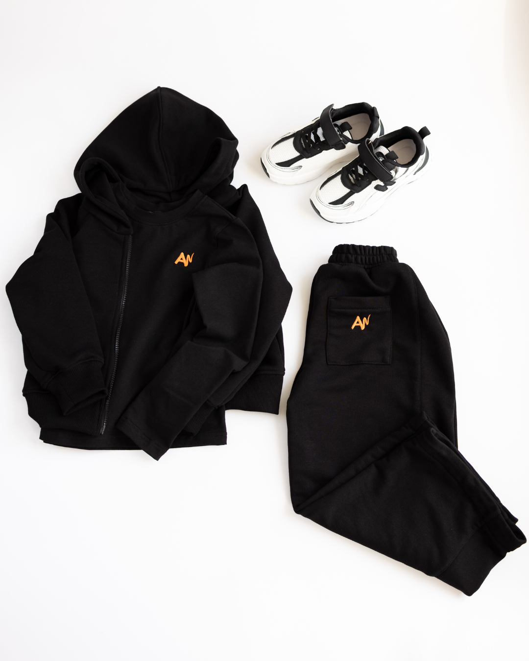 Black kids tracksuit set by Alwair Kids with sneakers laid out on white background