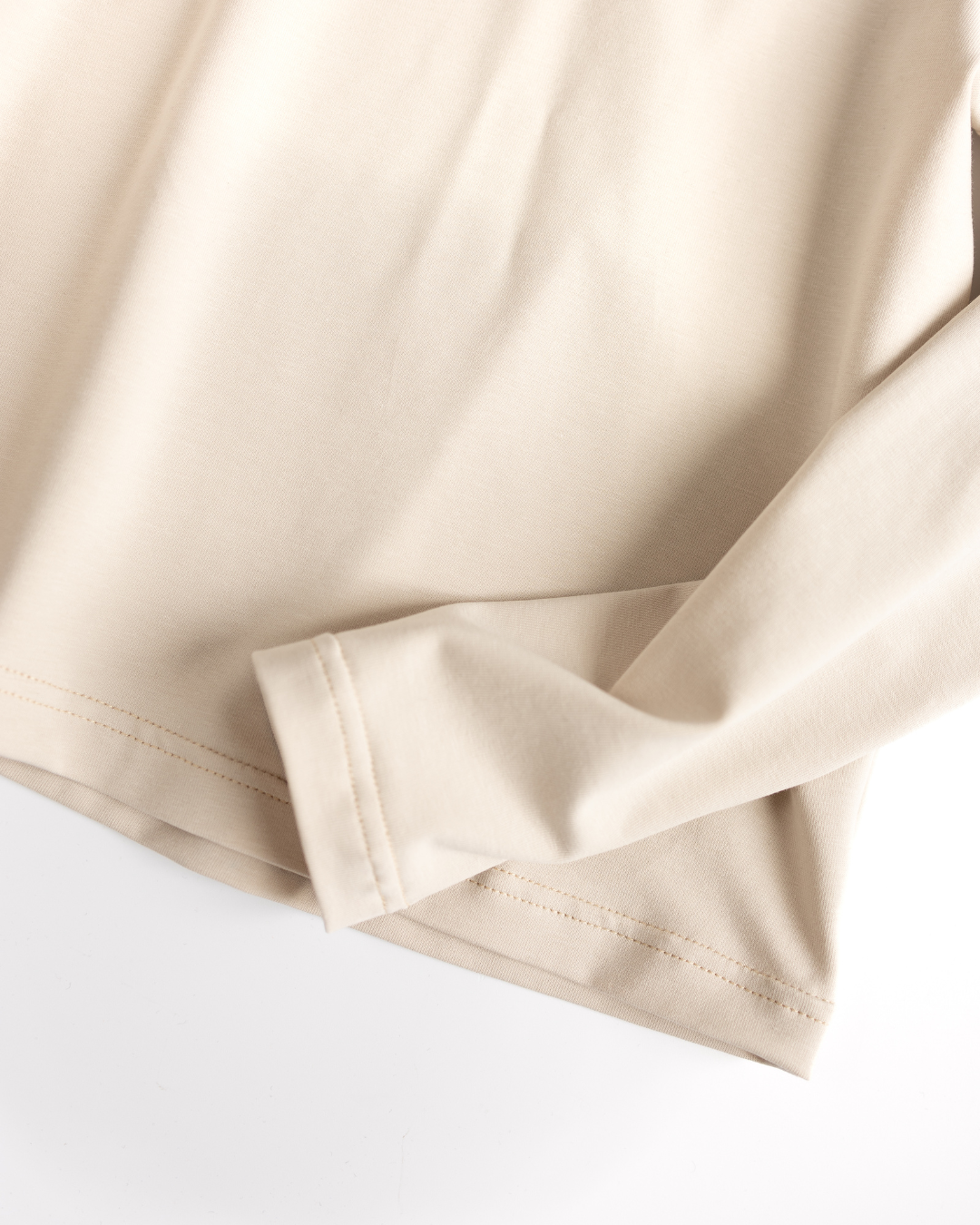 Detailed stitching of sleeve and hem on beige cotton longsleeve

