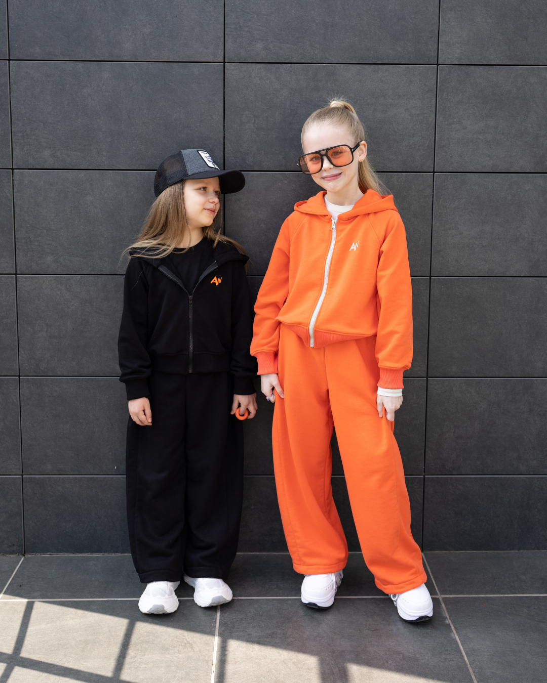 Girls wearing Alwair Kids Dolce Bambina tracksuits in black and orange