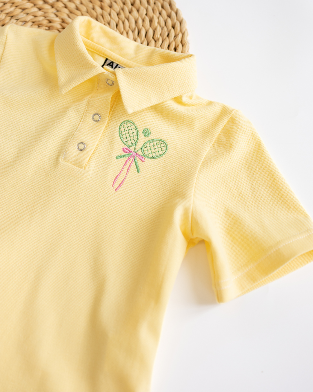 Close-up of embroidered tennis design on yellow kids polo shirt