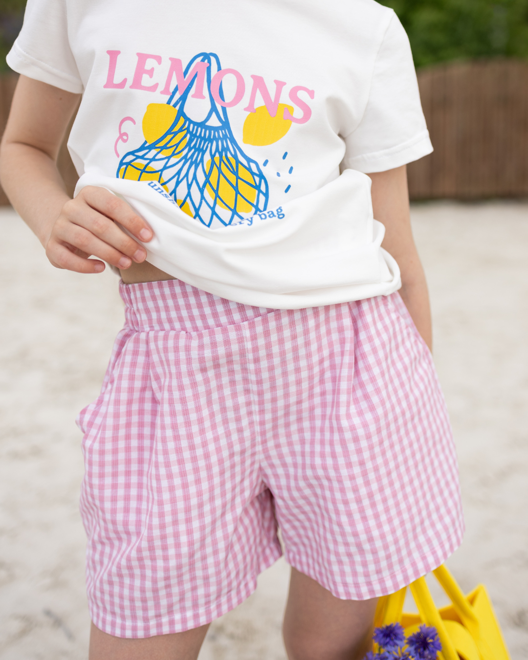 Girl wearing pink gingham check shorts with side pockets – lightweight summer kidswear, styled with graphic lemon t-shirt