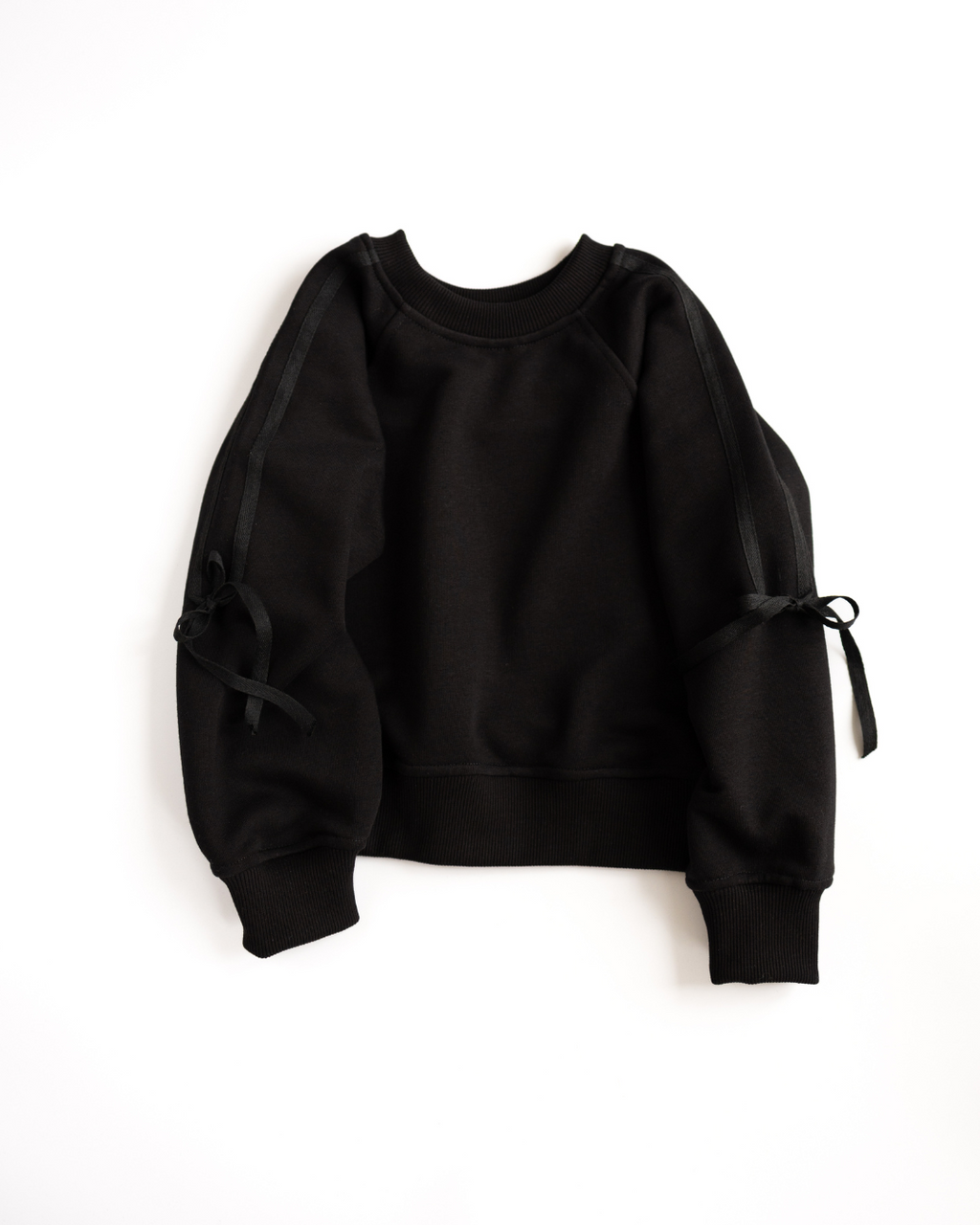 Black sweatshirt with black ribbon bows – minimal flat lay.