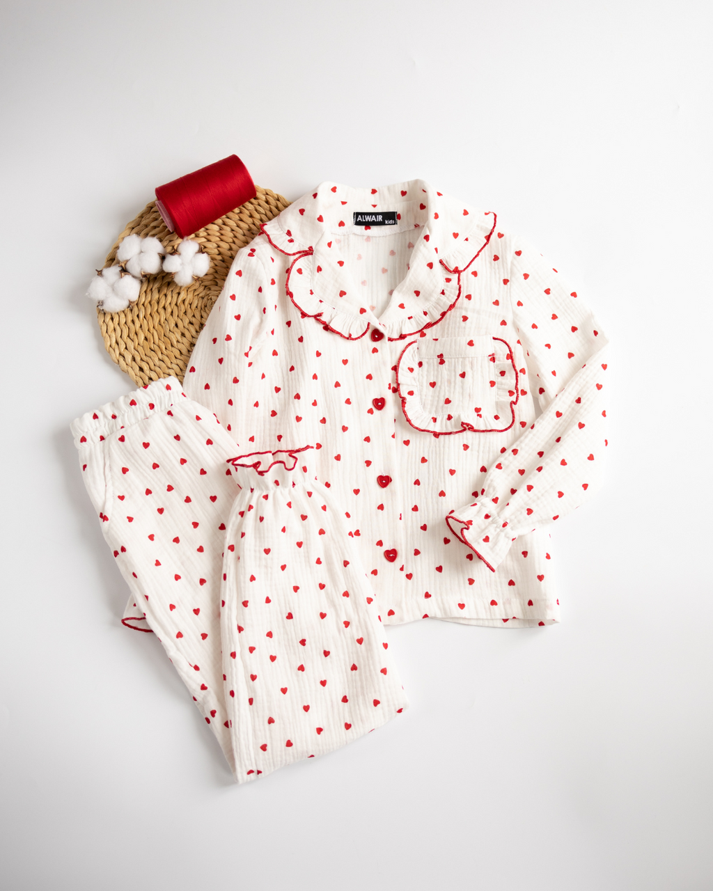 Styled flat lay of girls' muslin pajama set with cotton and red thread