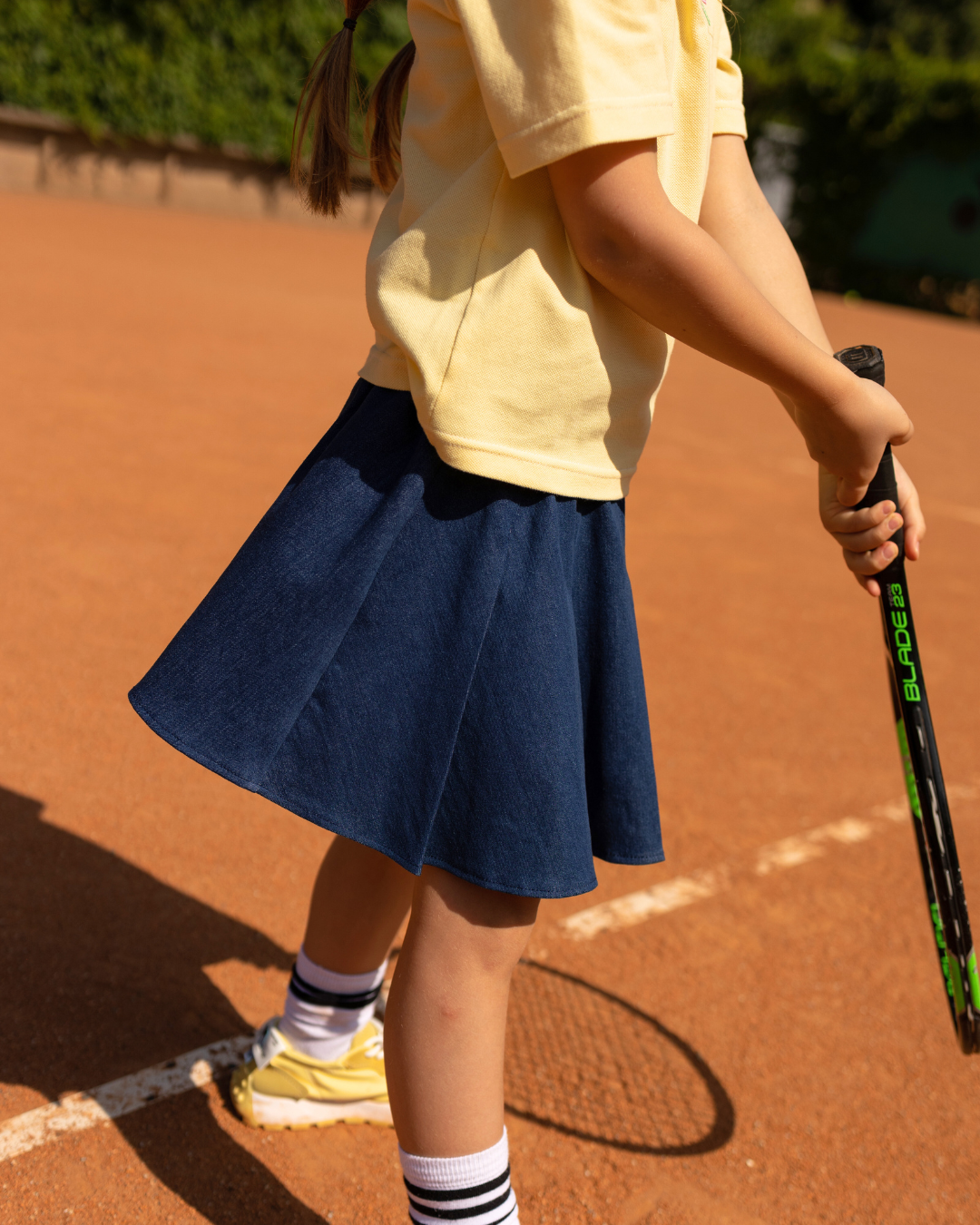 Close-up side view of tennis denim skirt in motion worn by girl on court