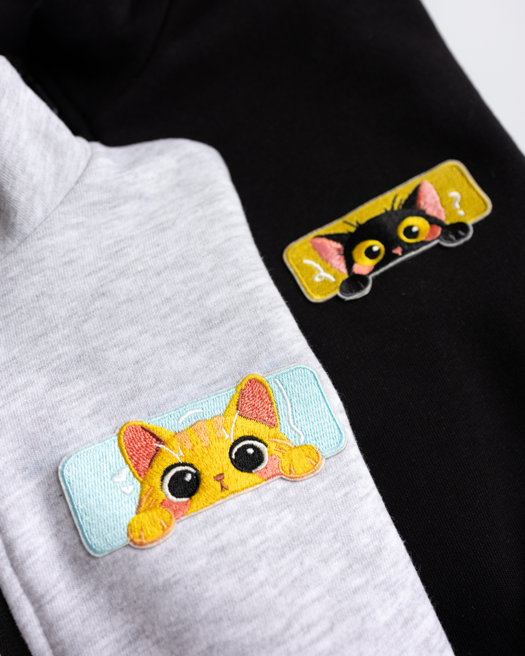 Close-up of embroidered cat patches on black and grey kids zip jackets