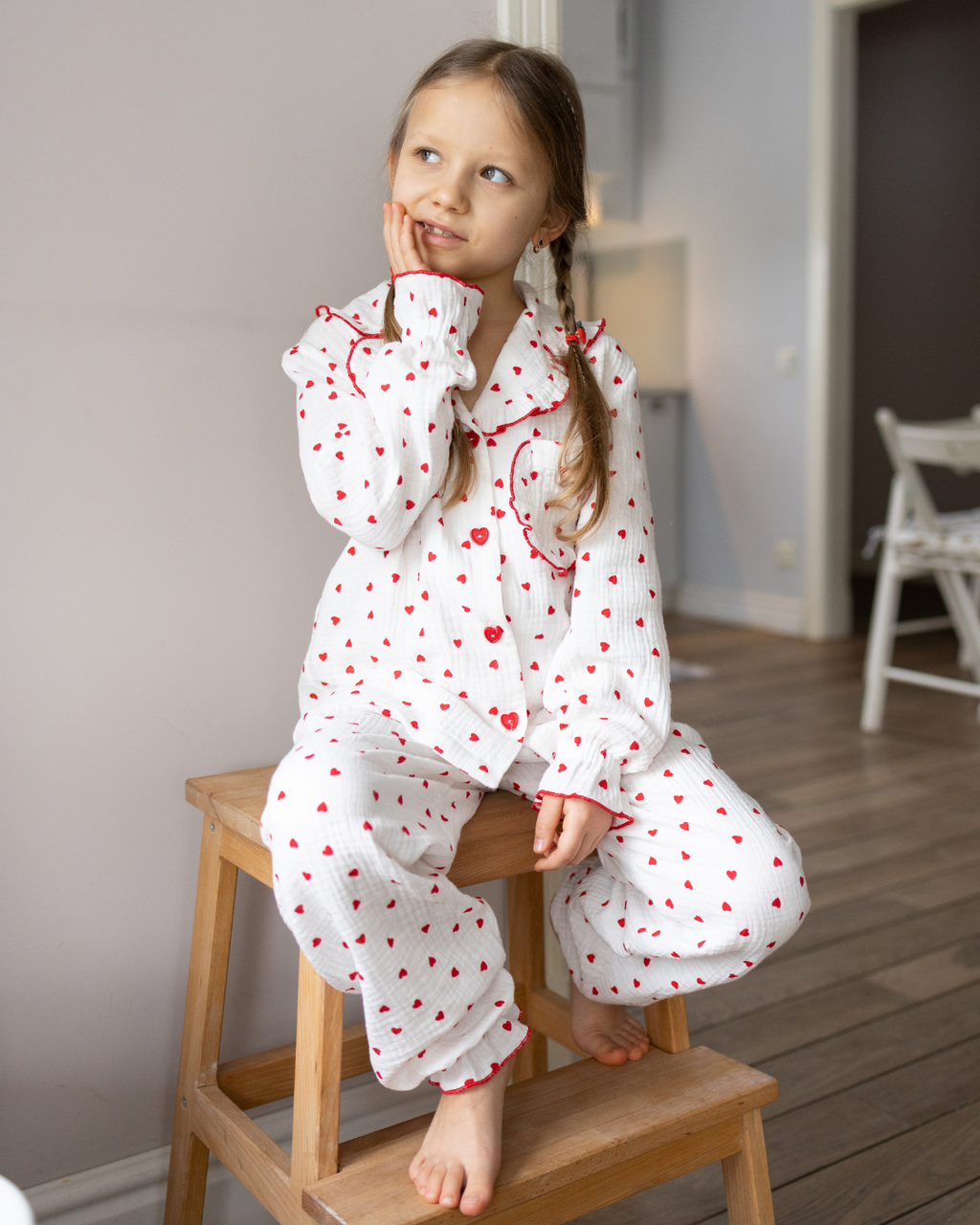 Girl wearing Alwair Kids muslin pajama set with red hearts, sitting on a wooden stool