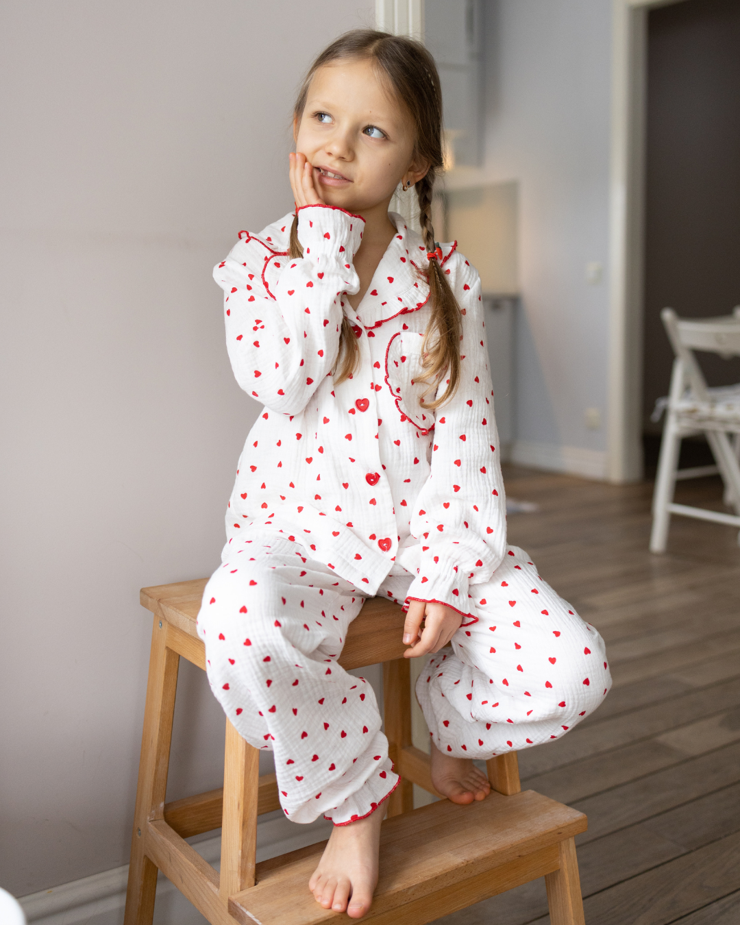 Girl wearing Alwair Kids muslin pajama set with red hearts, sitting on a wooden stool