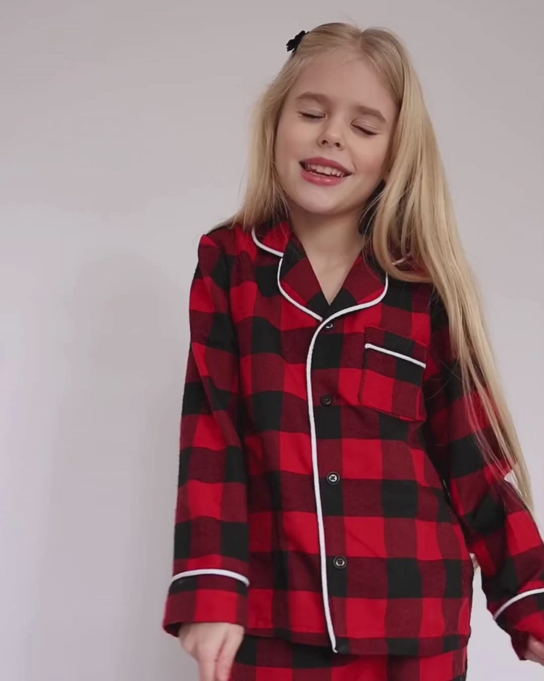 Video of a girl joyfully dancing in red plaid cotton pajamas by Alwair Kids, showing full outfit in motion on a white bed